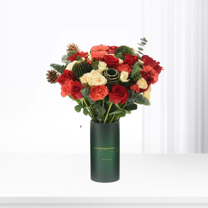 Vibrant red and cream roses, pinecones, and berries in festive green vase.