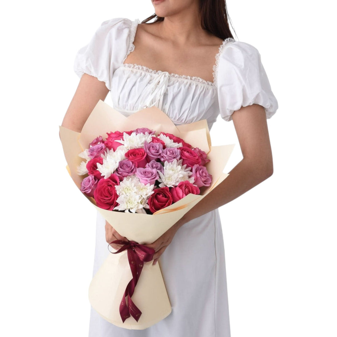 Woman holds vibrant pink, purple, and white rose bouquet wrapped in cream paper with burgundy ribbon.