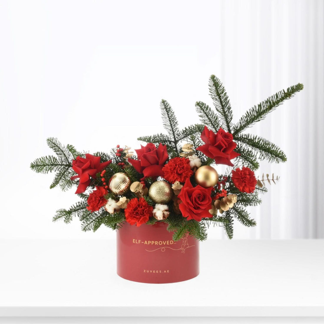Vibrant red roses, pine, gold ornaments in festive red box.