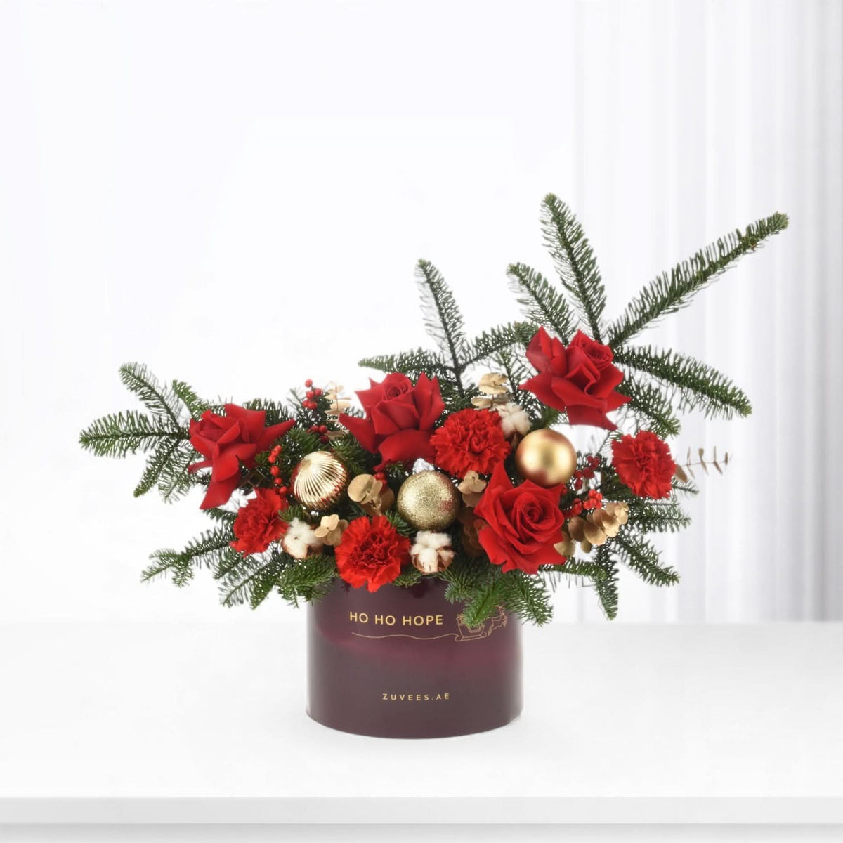 Rich red roses, carnations, and pine in deep burgundy vase with gold ornaments.