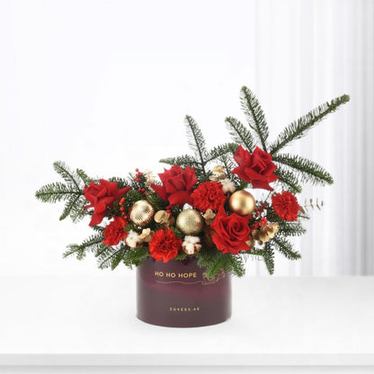 Rich red roses, carnations, and pine in deep burgundy vase with gold ornaments.