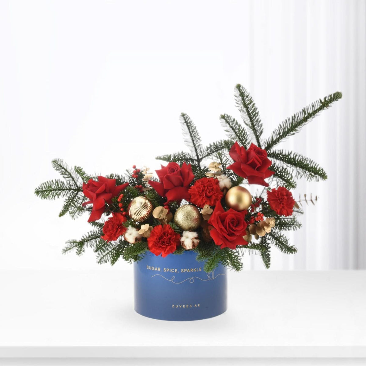 Vibrant red roses and carnations in festive blue box with gold ornaments and pine.