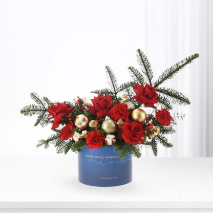 Vibrant red roses and carnations in festive blue box with gold ornaments and pine.