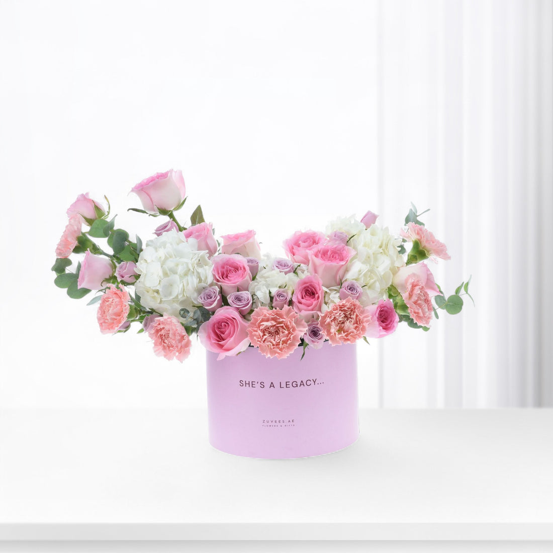 Pastel pink roses, carnations, and hydrangeas in a lavender box reading "She&