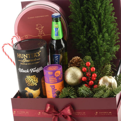 Rich burgundy gift box filled with festive treats, pine, ornaments, and a candy cane.