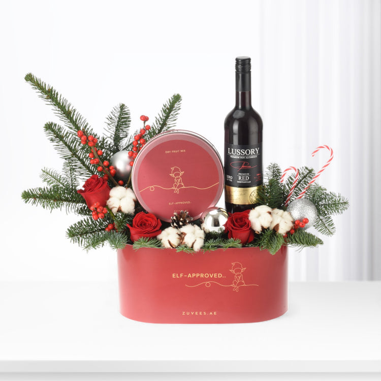 Red festive gift box with wine, candy canes, roses, and pine.