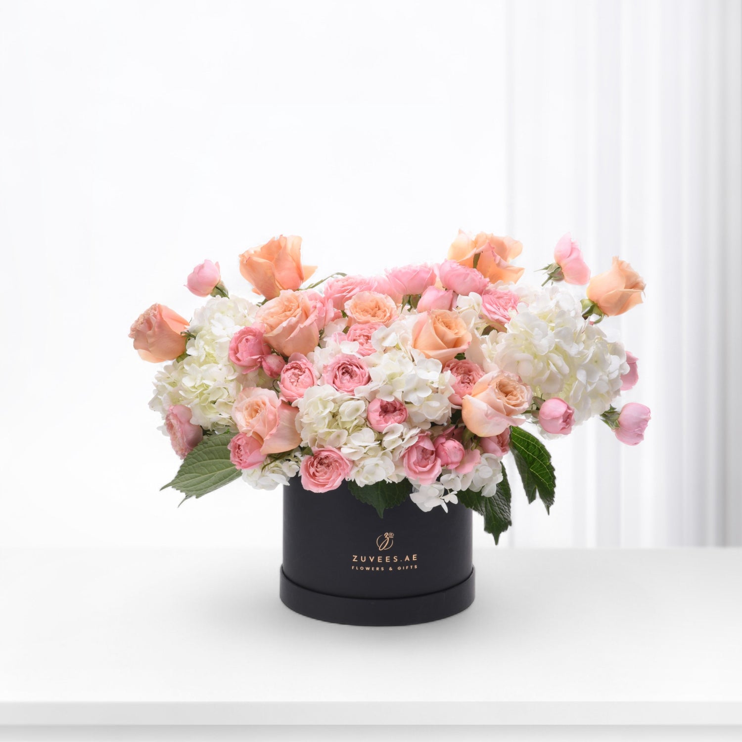 Elegant pink and peach roses with white hydrangeas in sleek black box.