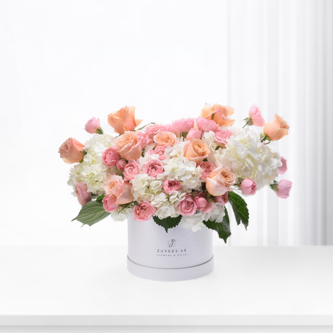 Pastel pink roses and white hydrangeas bloom elegantly in a branded white box.