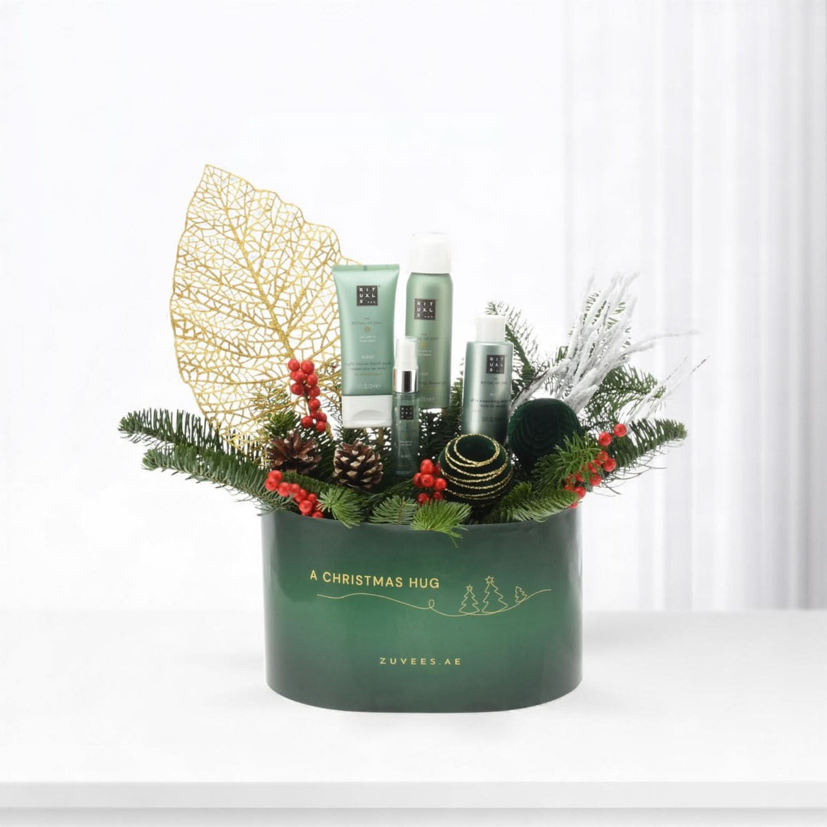 Green "A Christmas Hug" gift box with Rituals products, pine, berries, gold leaf, festive ornaments.