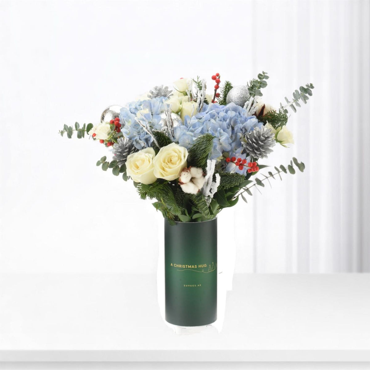 Elegant holiday bouquet in dark green vase with "A Christmas Hug" text.