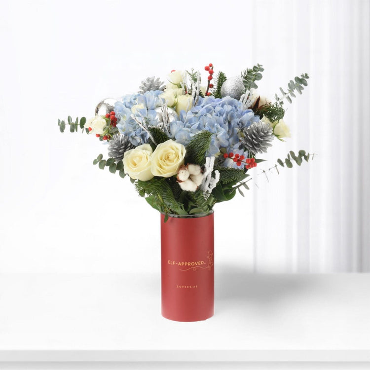 Red vase holds festive blue hydrangeas, white roses, pine, and silver ornaments.