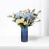 Blue vase holds snowy white roses, blue hydrangeas, silver pinecones, and red berries.