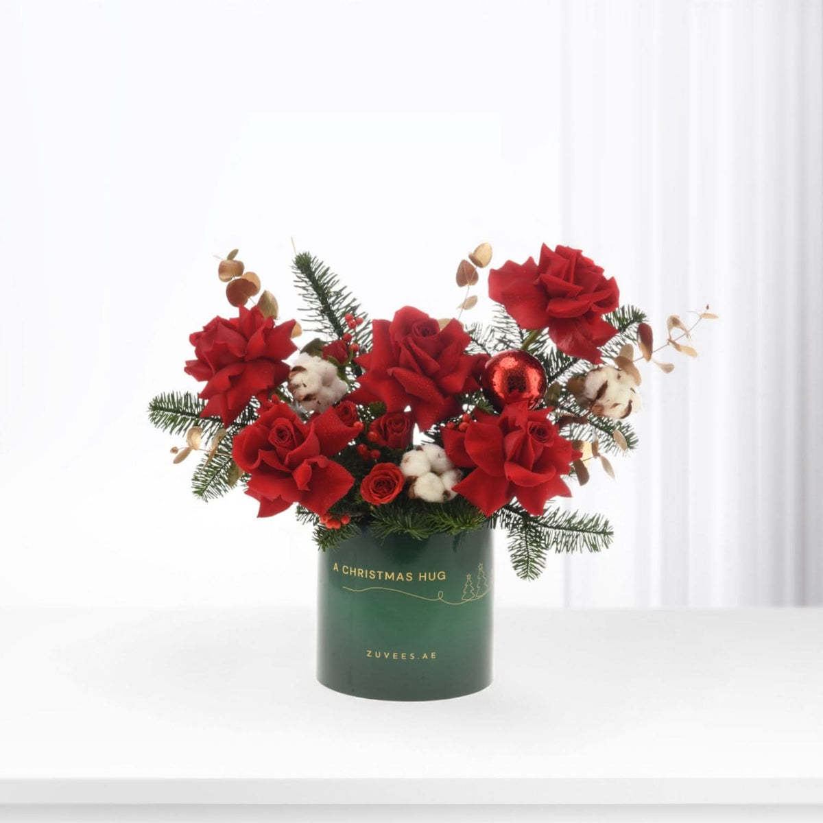 Vibrant red roses, cotton, pine, and gold accents in festive green vase.
