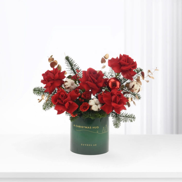 Vibrant red roses, cotton, pine, and gold accents in festive green vase.