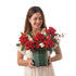 Woman holds festive red rose bouquet in green "Christmas Hug" box.
