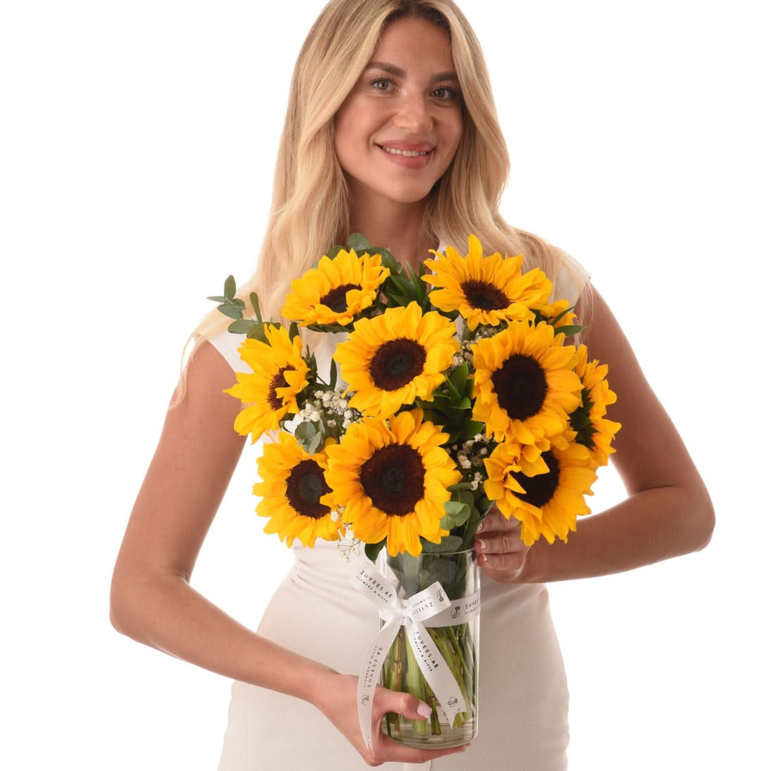 Vibrant sunflowers in clear glass vase with white ribbon, held by smiling woman.