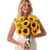 Vibrant sunflowers in clear glass vase with white ribbon, held by smiling woman.