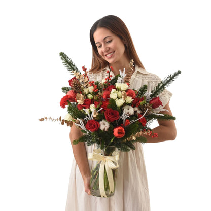 Woman smiles holding festive red and white floral arrangement in glass vase.