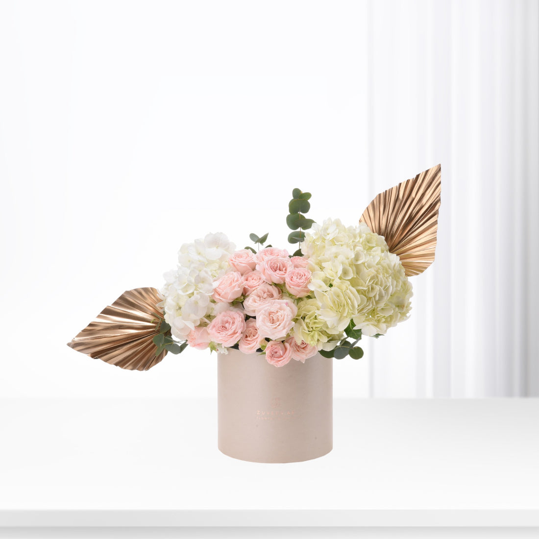 Soft pink roses and hydrangeas in beige vase with gold leaf accents.