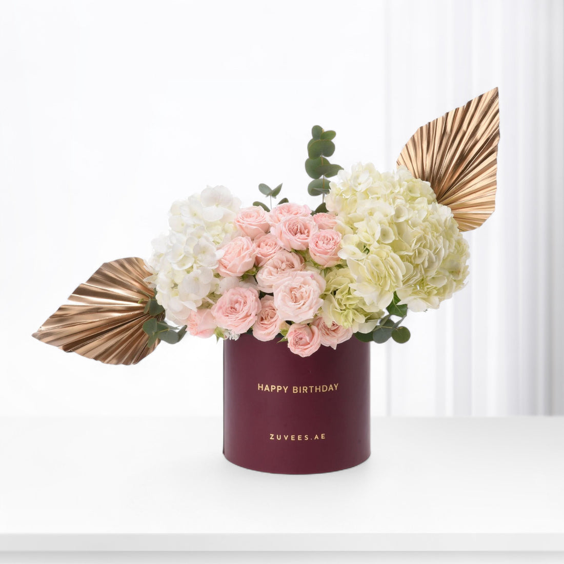 Elegant burgundy vase with gold "Happy Birthday" text, pink roses, white hydrangeas, and metallic gold leaves.