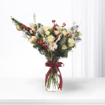 Elegant Christmas bouquet with white roses, red berries, gold ornaments, and fir in clear vase with burgundy ribbon.