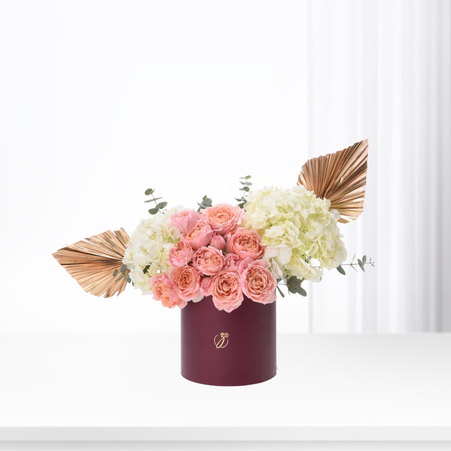 Elegant burgundy box holds blush roses and cream hydrangeas, accented with gold fan leaves.