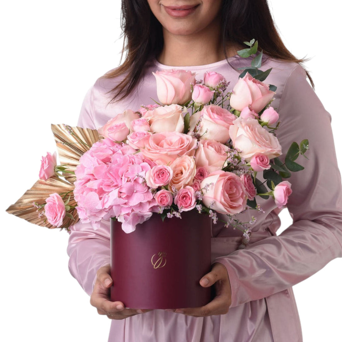 Elegant pink roses and hydrangeas in burgundy hat box, held by smiling woman.