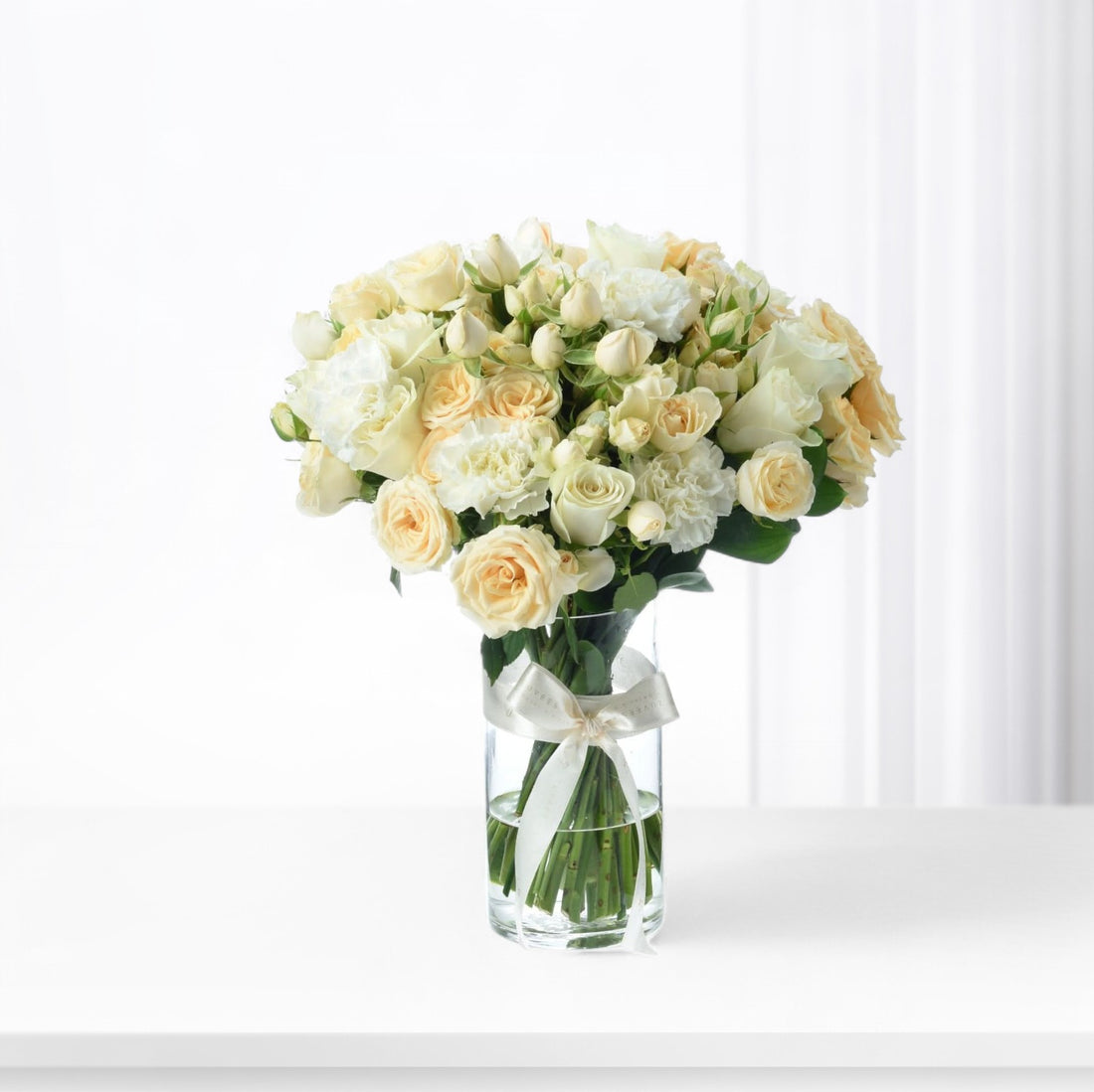 Elegant white and cream roses and carnations in clear vase with satin bow.