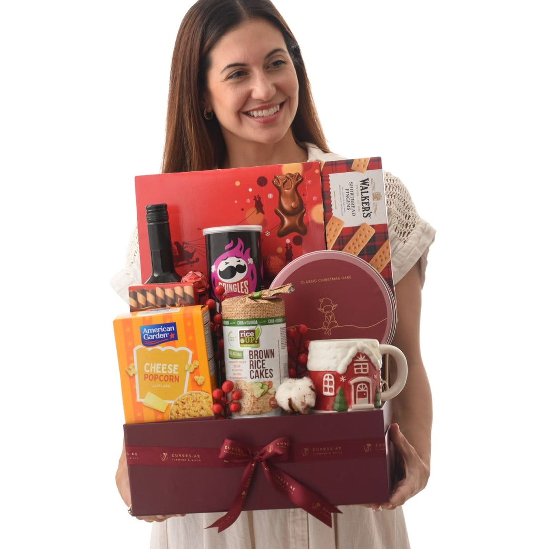 Woman holds festive gift basket with red bow, featuring popcorn, cake, crackers, and mug.
