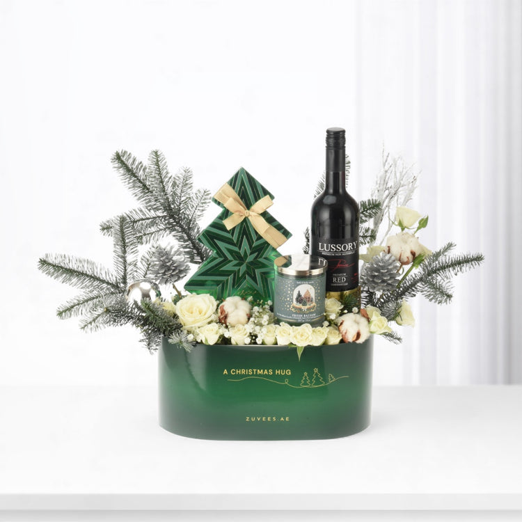 Green gift basket with white roses, pine, candle, and wine bottle.