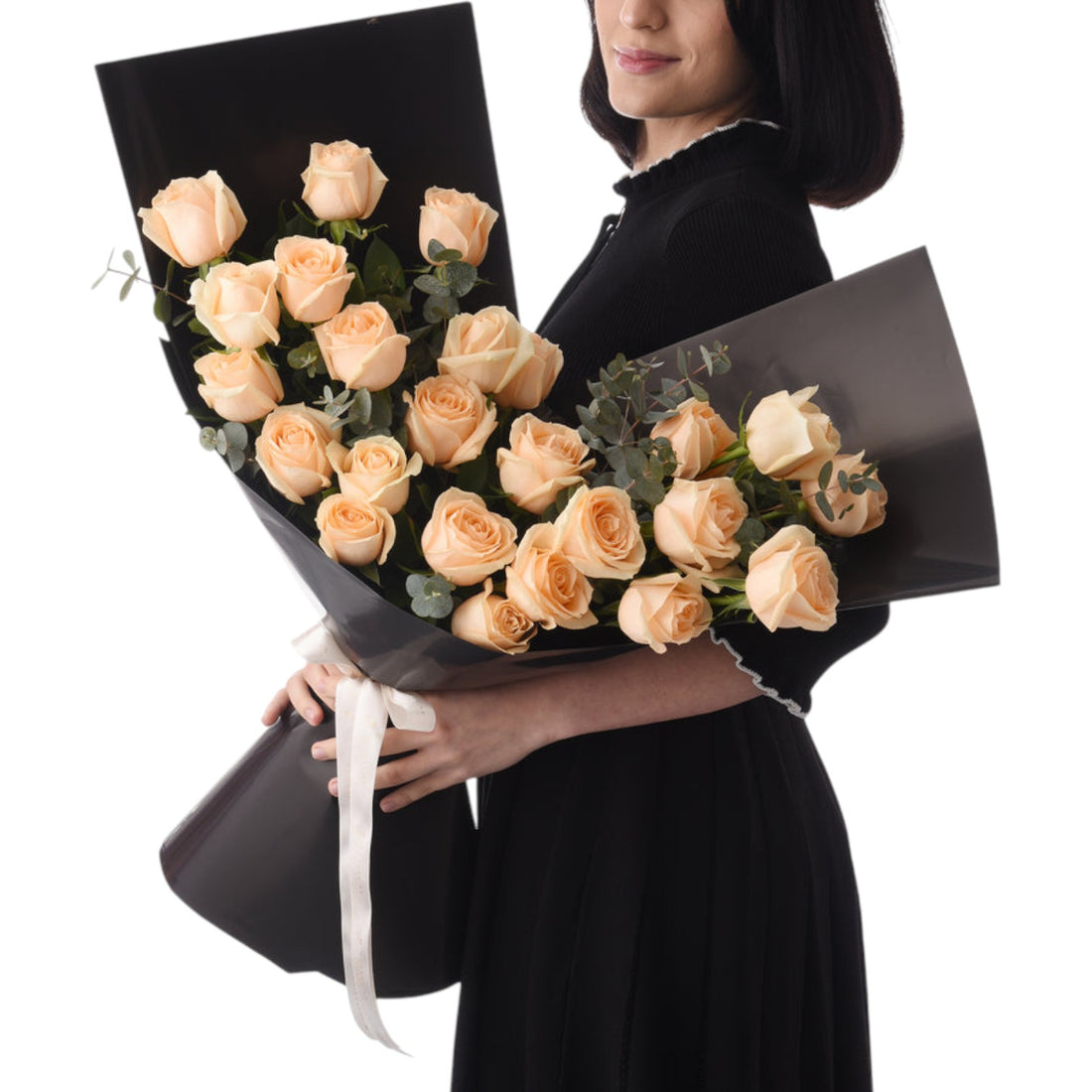 Elegant woman holds peach rose bouquet in sleek black wrap with white ribbon.