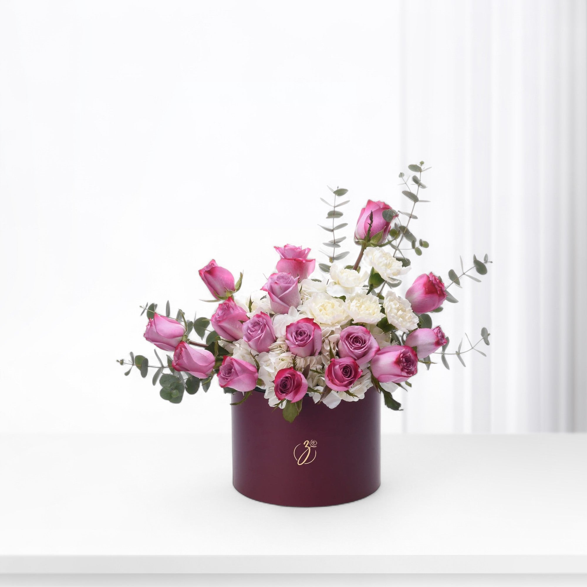Elegant burgundy box holds vibrant pink roses and white blooms with eucalyptus.