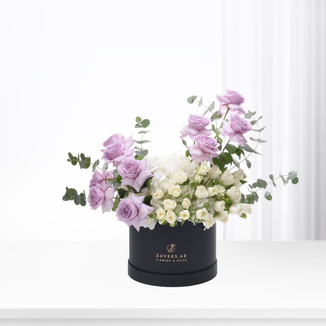 Elegant lavender roses and white blooms in sleek black box.