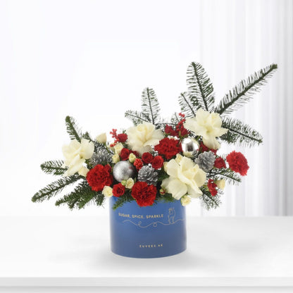 Vibrant red and cream blooms with pine, silver ornaments, and festive blue container.