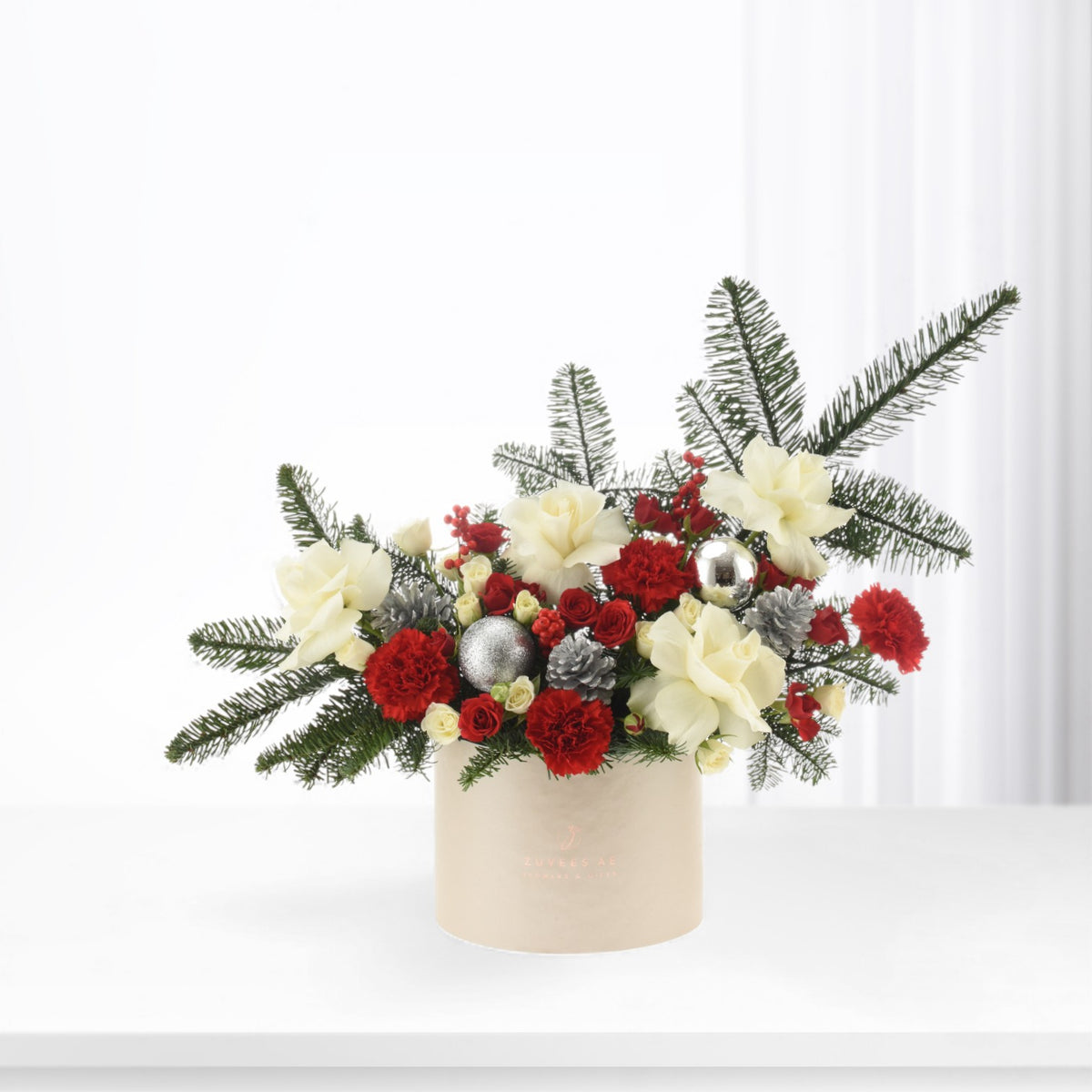 Elegant holiday floral arrangement in beige box with red, white blooms and silver ornaments.