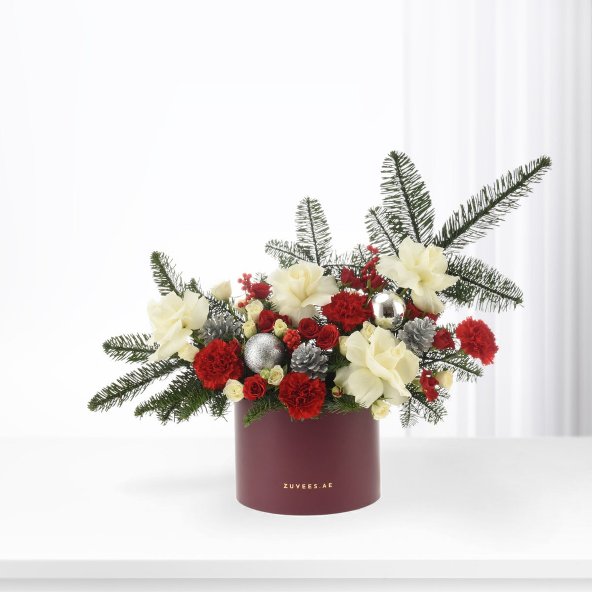 Vibrant red and cream floral arrangement in burgundy box with pine and ornaments.