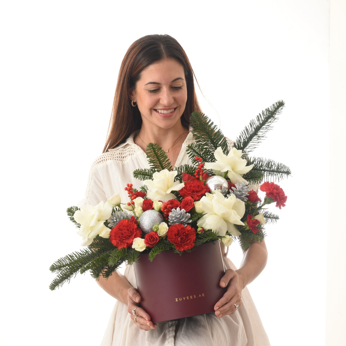 Woman holds festive red and white floral arrangement in burgundy box.
