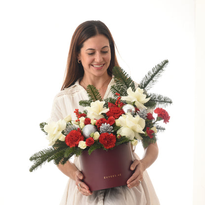 Woman holds festive red and white floral arrangement in burgundy box.
