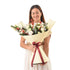 Woman smiles holding festive bouquet wrapped in cream paper with burgundy ribbon.