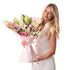 Blonde woman smiles holding pink-wrapped bouquet of roses and lilies.