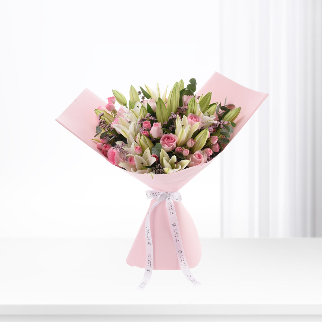Soft pink bouquet with roses and lilies, elegantly wrapped in pastel paper.