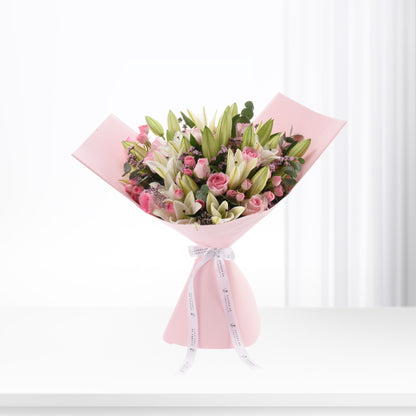 Soft pink bouquet with roses and lilies, elegantly wrapped in pastel paper.