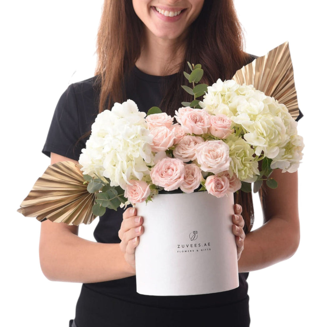 White cylindrical box holds blush roses and ivory hydrangeas, accented with gold fan leaves.