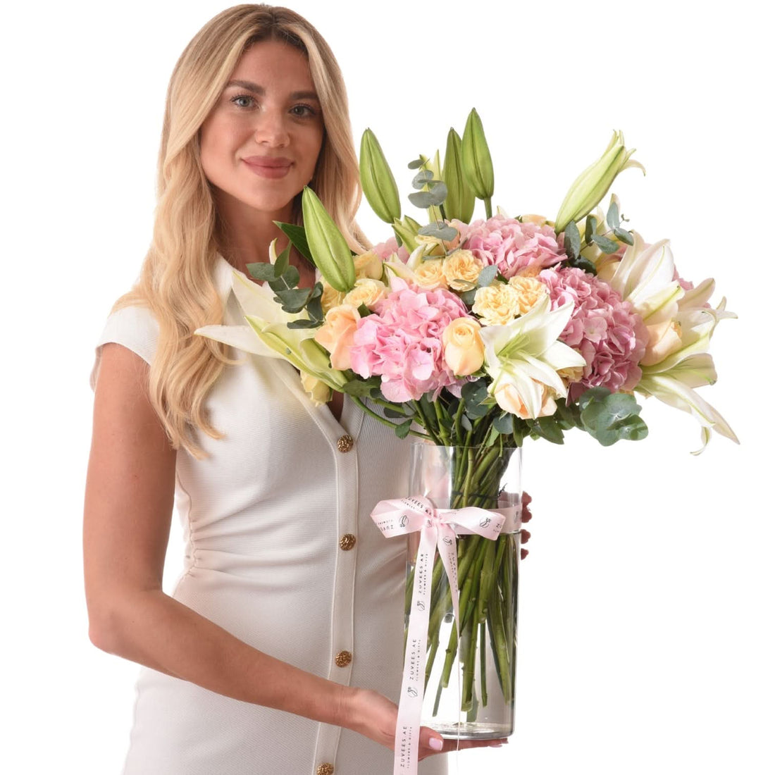 Woman holds pastel floral arrangement in clear vase with branded ribbon.