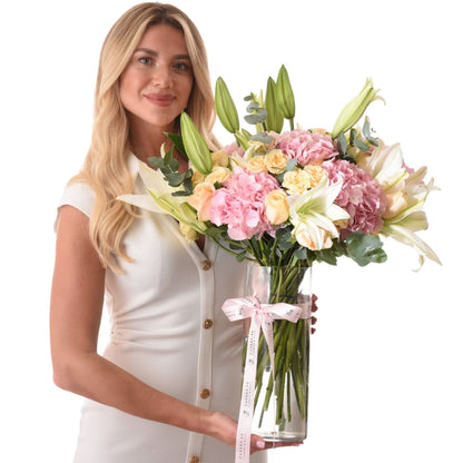 Woman holds pastel floral arrangement in clear vase with branded ribbon.