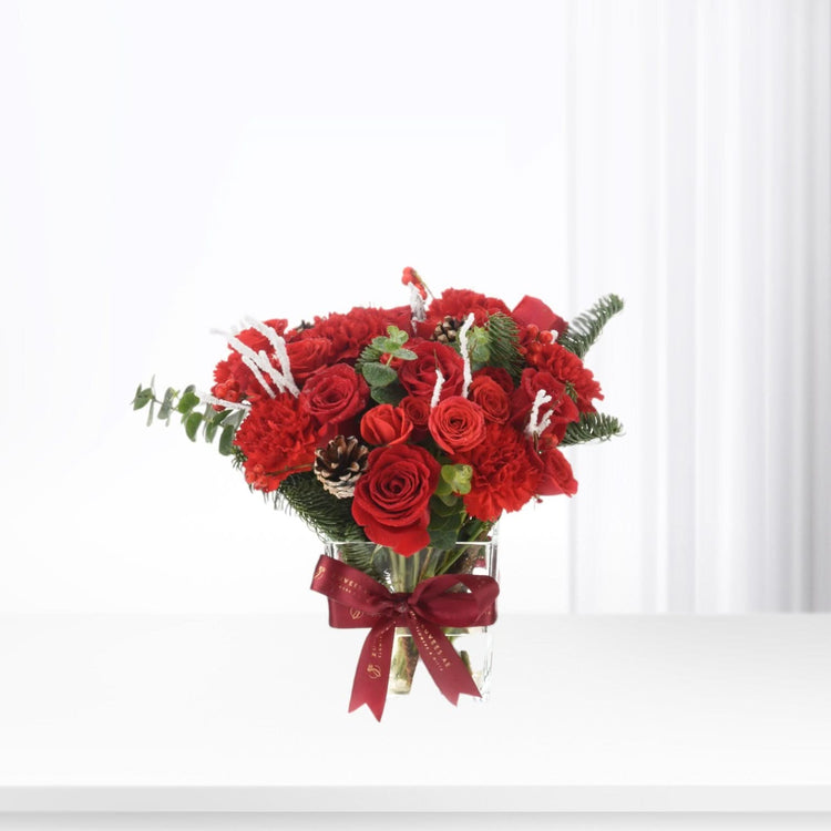 Vibrant red roses and carnations in glass vase with burgundy bow.