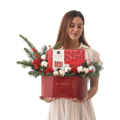 Woman holds festive red gift box adorned with pine, roses, and candy canes.
