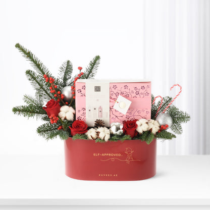 Festive red gift box with roses, pine, ornaments, and pink skincare set inside.