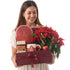 Woman smiles holding festive red gift box with poinsettias, cake, coffee, and mug.