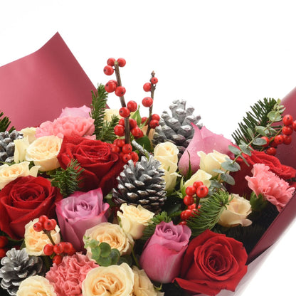 Vibrant holiday bouquet with red roses, berries, pinecones, and pink carnations wrapped in deep red paper.